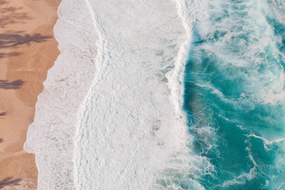 Stunning aerial view capturing waves crashing onto a sandy beach, showcasing the power of nature.