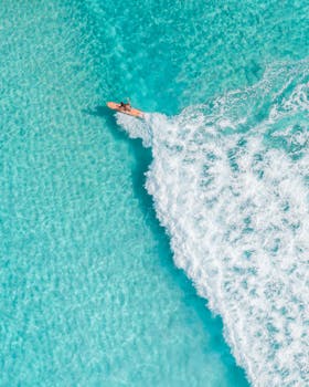 航拍镜头下，一名冲浪者在清澈碧绿的海水中乘风破浪，展现了自然美景