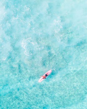 Aerial shot of a surfer paddling in vibrant blue waters of Hawaii, showcasing the beauty of ocean adventure.