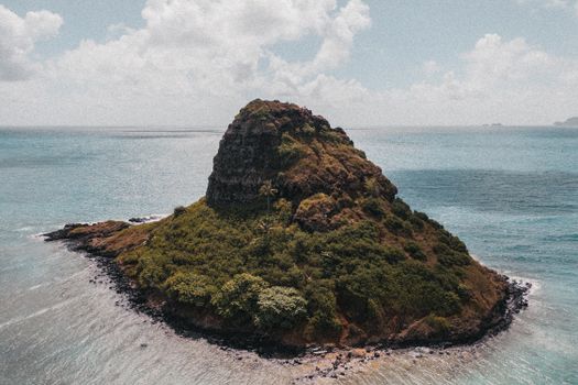 Aerial shot of a lush, rocky island surrounded by the serene ocean under a cloudy sky.