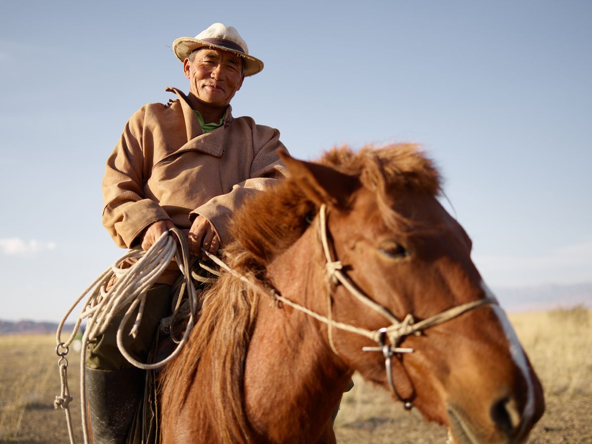 A Mongolian horseman riding across the wide-open grassland steppe