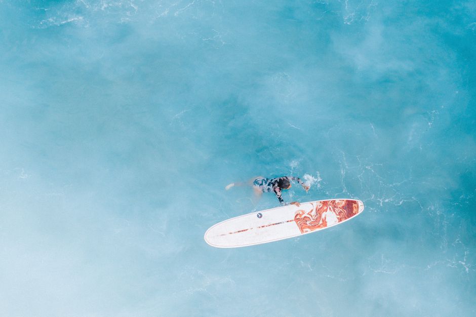 Aerial shot of a surfer floating with a board on the tranquil ocean waves. Perfect for ocean lifestyle themes.