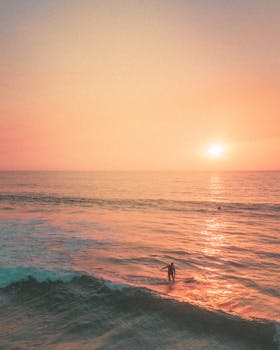 A lone surfer riding waves at sunset on a Hawaiian beach, creating a tranquil scene.