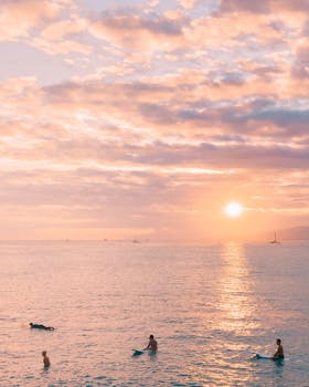 Surfers enjoying a serene sunset over the ocean in Hawaii, creating a peaceful and stunning beach scene.