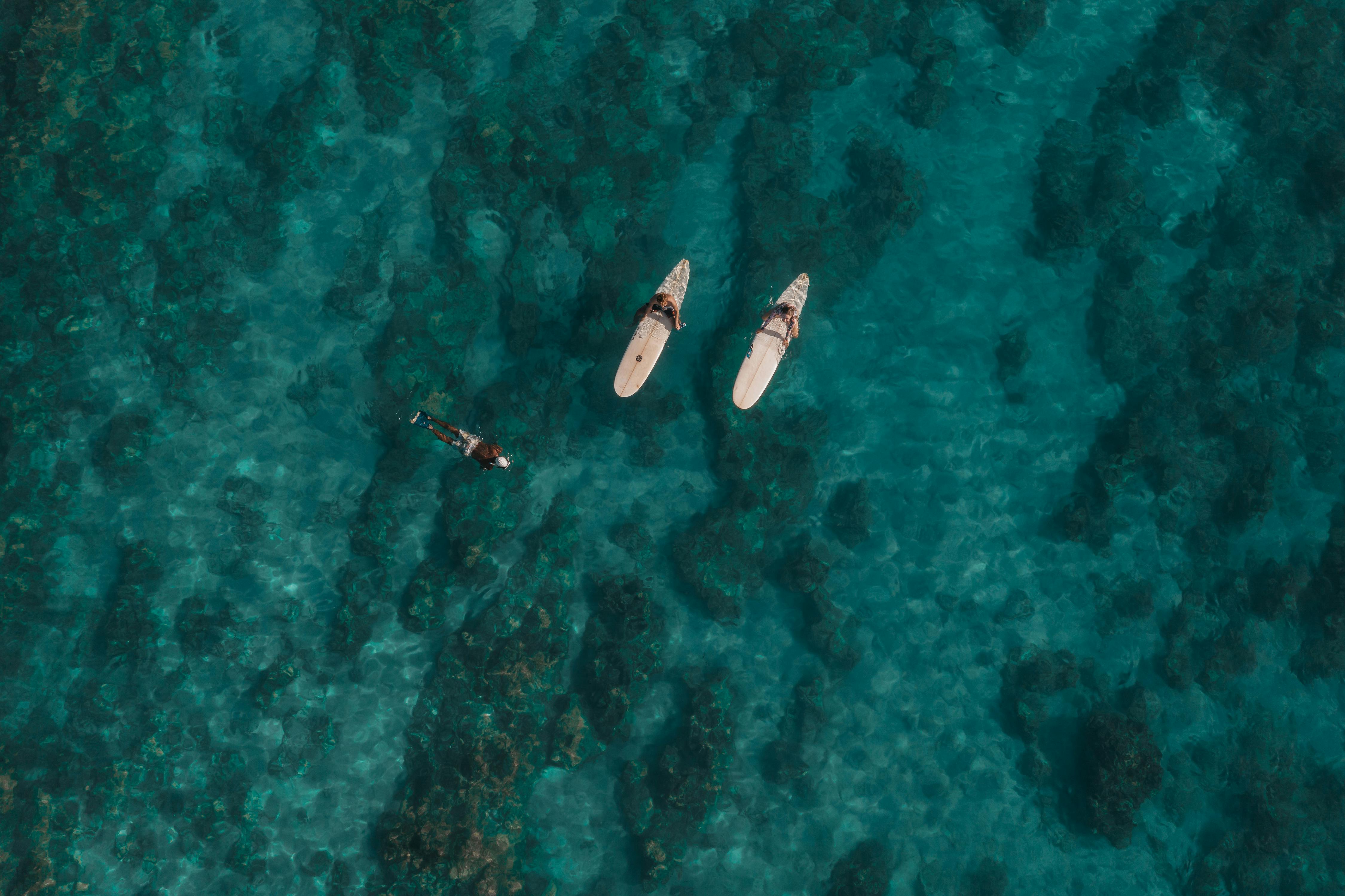 A stunning aerial shot of surfers paddling in the crystal clear waters off the coast of Hawaii.