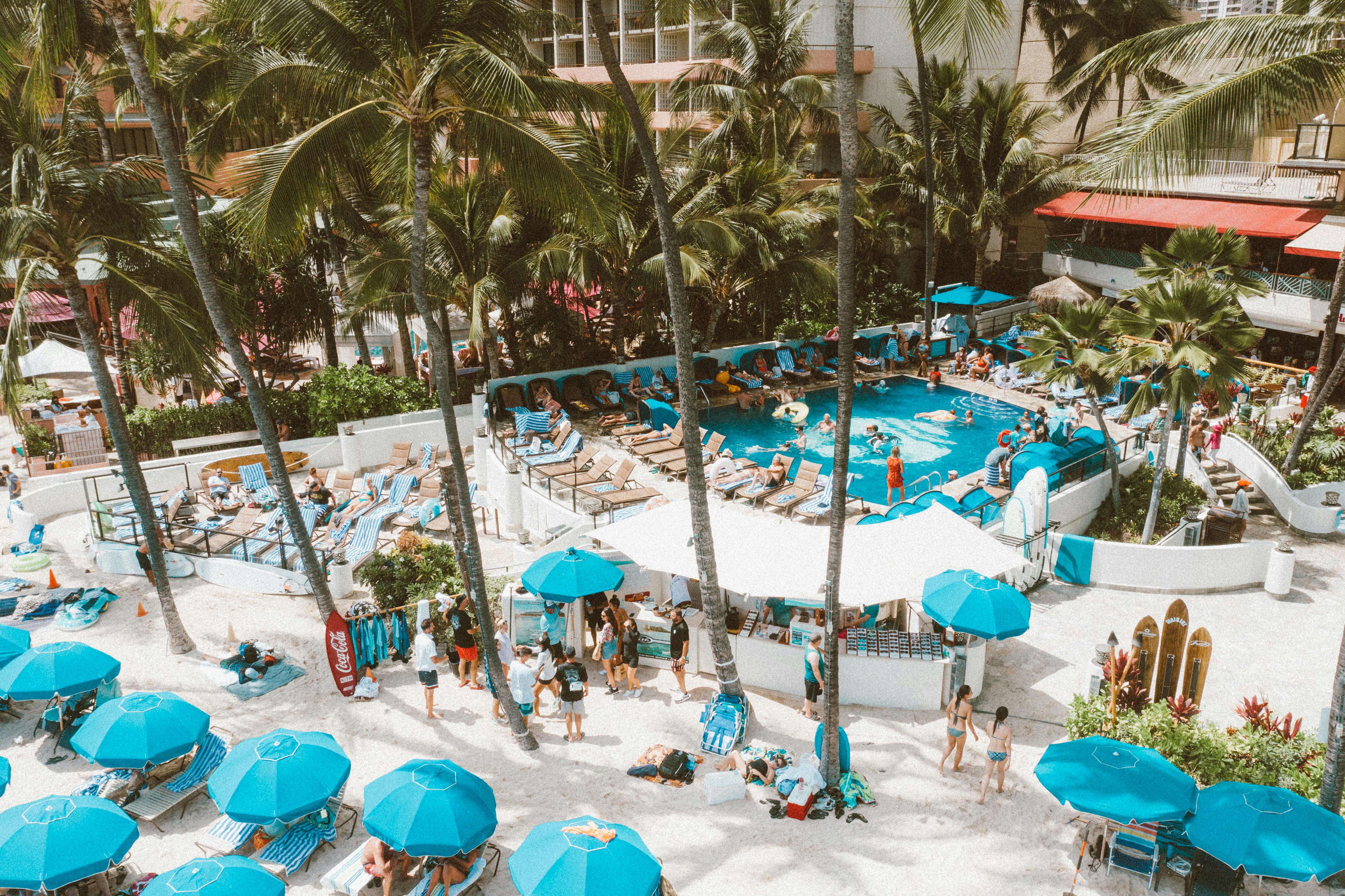 Aerial view of a luxurious resort pool surrounded by palm trees and beach umbrellas in Waikiki, Oahu.