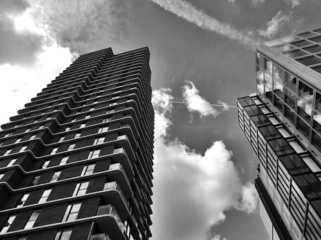一张引人注目的黑白照片以低角度拍摄，展现了多云天空下的城市摩天大楼