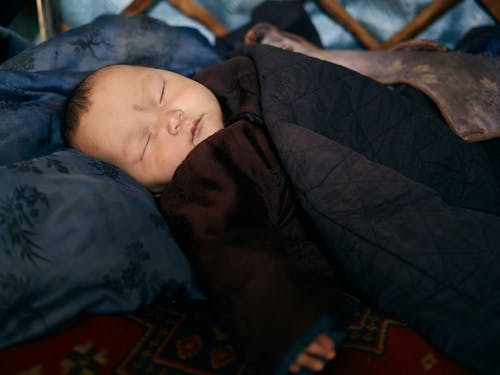 Side view of closeup Asian infant sleeping in warm national clothes under blanket on pillow on carpet