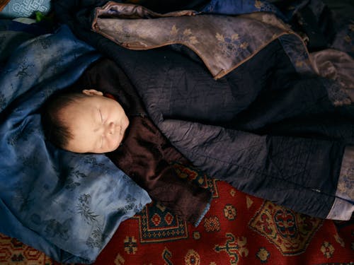 Sleeping ethnic baby in traditional clothes under jacket of adult man