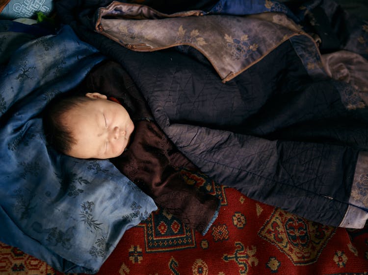 Sleeping Ethnic Baby In Traditional Clothes Under Jacket Of Adult Man