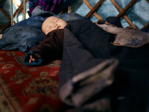 Free Full length Asian infant lying on carpet while sleeping in warm national clothes under blanket Stock Photo