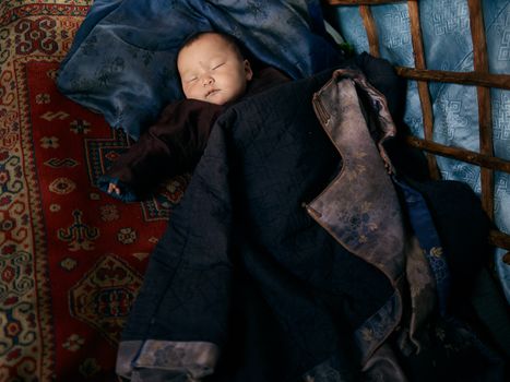 从上方看，一个全身熟睡的亚洲婴儿穿着保暖衣服躺在地毯上，外面套着一件带花卉衬里的成人男士夹克
