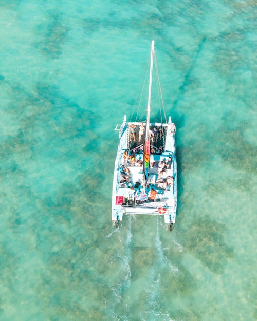 Drone view of white sail boat with passengers cruising in turquoise transparent calm sea with coral reefs