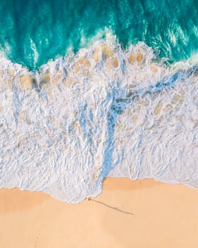 A captivating aerial shot of turquoise ocean waves crashing onto a sandy beach.