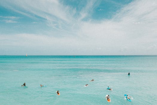 Aerial view of surfers on turquoise ocean waves in Hawaii with clear skies.