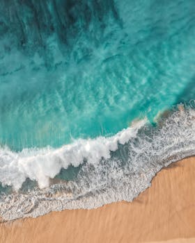 Stunning aerial photo of turquoise waves crashing onto a sandy beach, capturing natural beauty and surf essence.