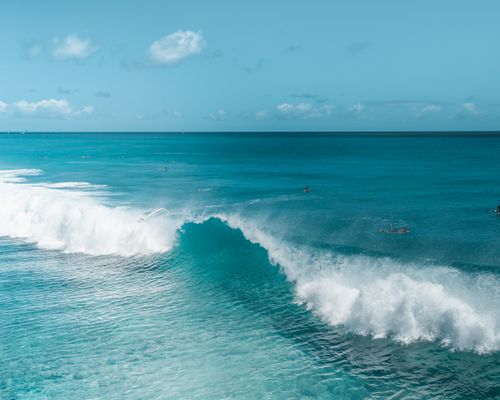 Free Aerial view of surfers riding waves in a vibrant blue ocean under a clear sky. Stock Photo