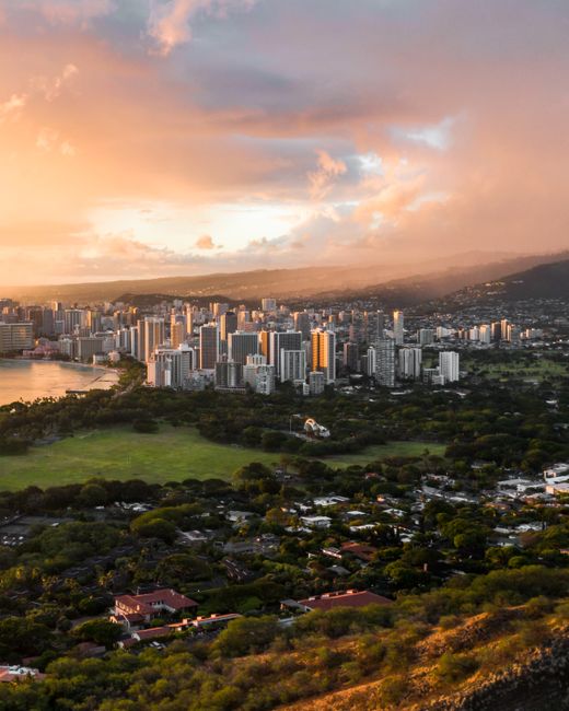 Photo by Jess Loiterton Stunning aerial view of Honolulu skyline under a vibrant sunset sky in Hawaii.