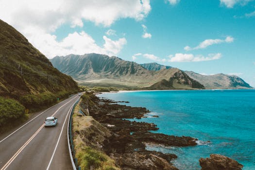 Photo by Jess Loiterton A stunning aerial view of a coastal road in Hawaii, featuring ocean and mountains.