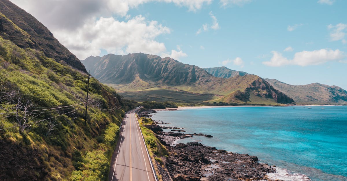 Photo by Jess Loiterton Aerial view of the scenic coastline and roadway in Waianae, Hawaii with lush mountains and turquoise ocean.