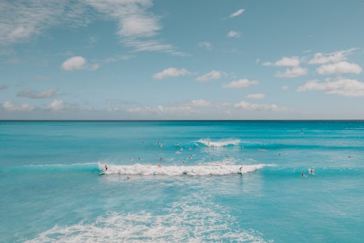 Drone shot of surfers riding waves in blue Hawaiian ocean under a clear sky.