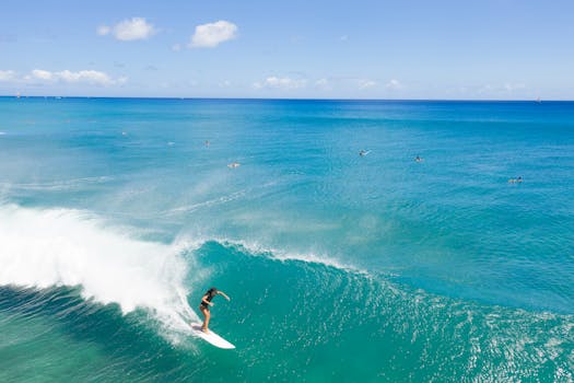 A breathtaking aerial view of a surfer catching waves on a sunny Hawaii beach.