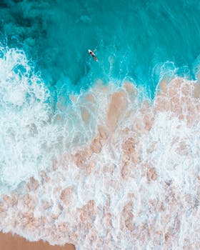 Stunning aerial view of a surfer riding waves on a turquoise beach in Honolulu, Hawaii.