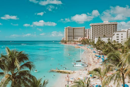 A lively scene at Waikiki Beach, Honolulu with turquoise waters and vibrant beachgoers under a bright blue sky.