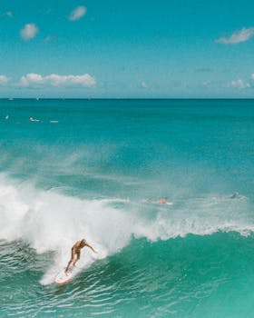 Dynamic aerial shot of a surfer riding waves in Hawaii's turquoise waters.