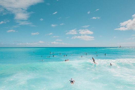 A lively tropical beach scene with surfers enjoying the turquoise ocean waves under a clear blue sky.