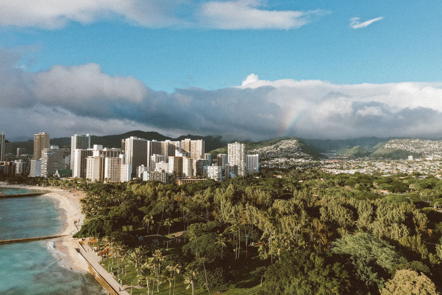 A stunning aerial view of Honolulu with skyscrapers, coastline, and lush greenery under a vibrant sky.