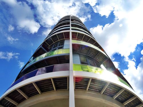 Free Low angle view of a modern skyscraper with colorful glass panels and a bright blue sky. Stock Photo