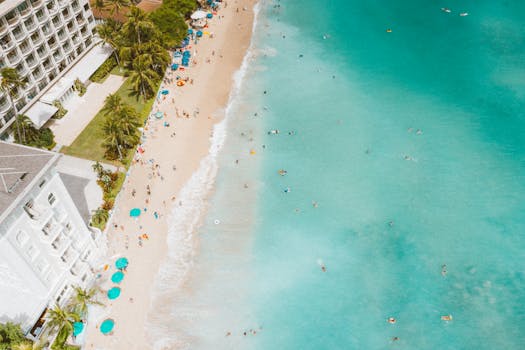 Aerial view of Waikiki Beach in summer with beachgoers and turquoise ocean.