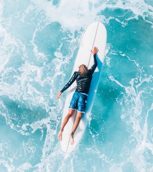 An aerial shot of a surfer lying on a surfboard amidst turquoise ocean waves, showcasing a tranquil moment.