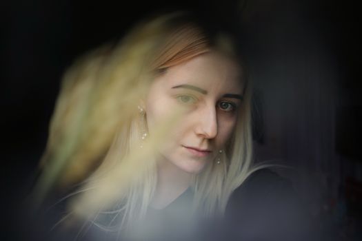 这幅肖像画描绘了一位年轻女子，她正透过柔和灯光的窗户若有所思地凝望，画面宁静