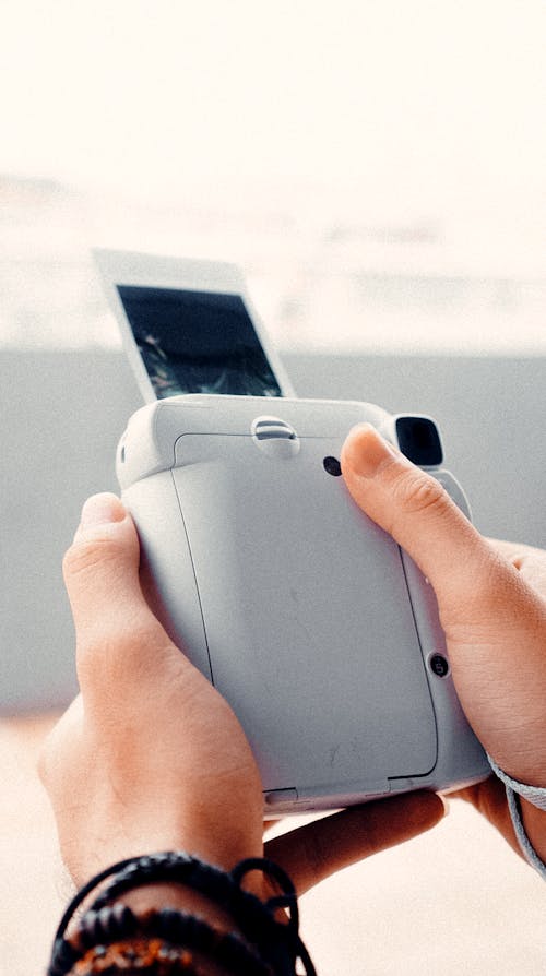 High angle of crop anonymous person with bracelets printing photo with modern instant camera on sunny day