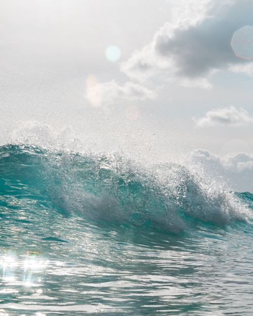 Free Dynamic ocean waves crashing with sunlit reflections and a partly cloudy sky. Stock Photo