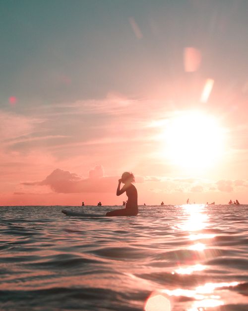 Free Silhouette of a surfer at sunset on calm ocean waters, reflecting warm hues. Stock Photo