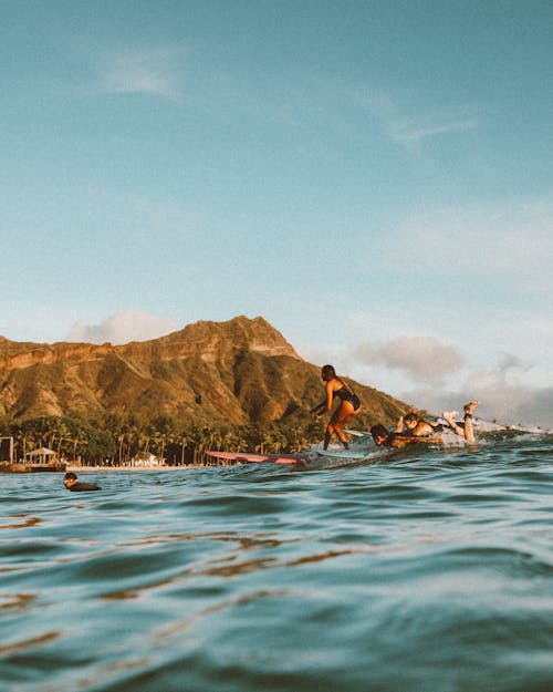 People Swimming on Sea Near Mountain