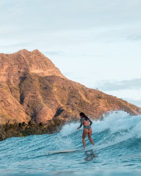 A surfer girl catching a wave against the backdrop of Diamond Head in Hawaii during a sunny day.