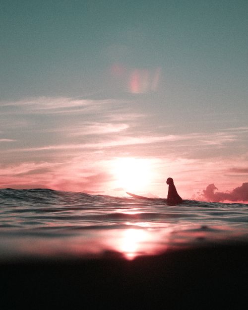 Free A lone surfer silhouetted against a vibrant Hawaiian sunset over the ocean waves. Stock Photo