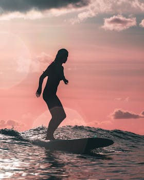 A silhouette of a woman surfing against a stunning pink sunset sky, capturing the beauty and leisure of Hawaii.