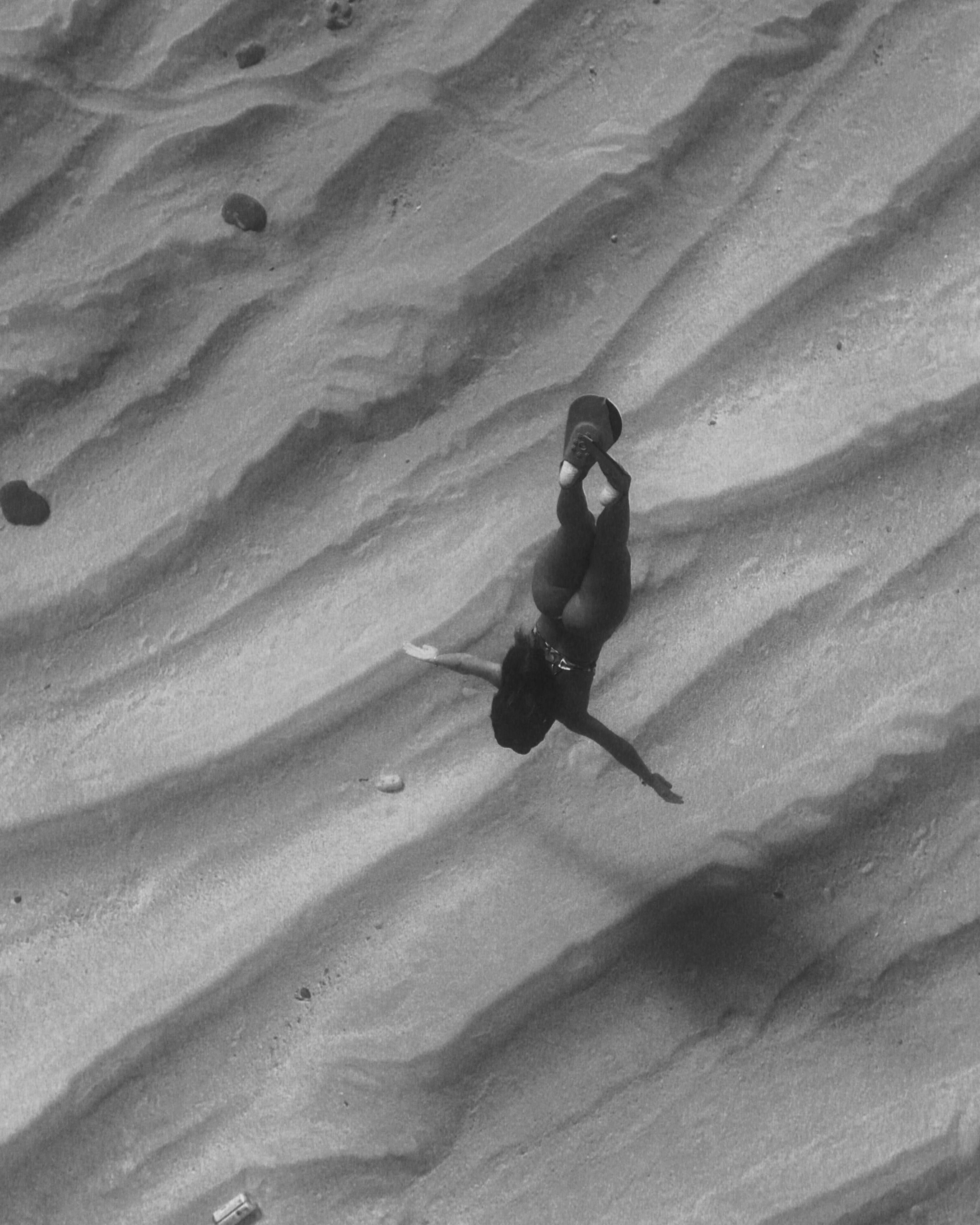 A woman gracefully swims underwater in a black and white image, capturing movement and texture.