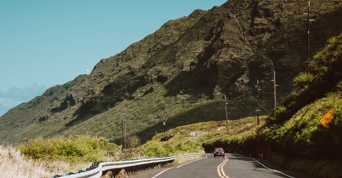 Photo by Jess Loiterton Curved road on Oahu, Hawaii with lush green mountains and clear blue skies, ideal for travel vibes.