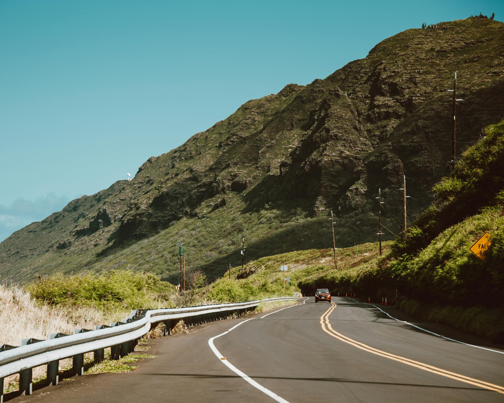 Curved road on Oahu, Hawaii with lush green mountains and clear blue skies, ideal for travel vibes.