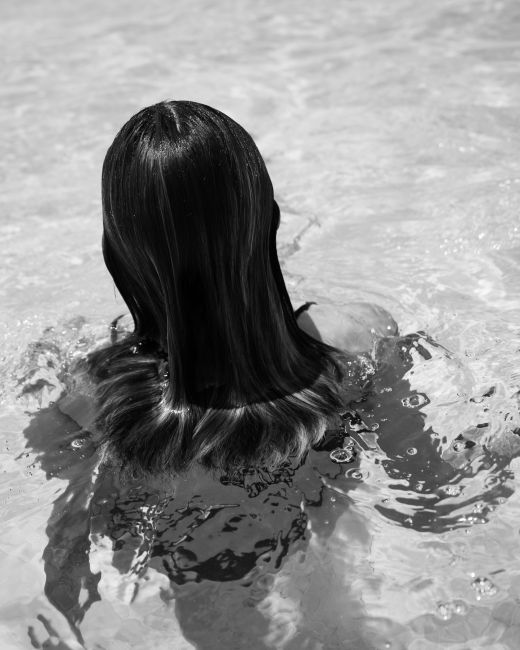 Black and white image capturing a woman with long hair swimming in clear water, creating a serene and peaceful mood.