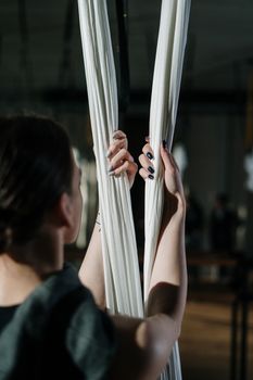A woman engages in aerial yoga, holding white silks in an indoor studio.