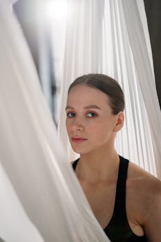 A woman gracefully poses with aerial yoga silks indoors, emphasizing focus and wellness.