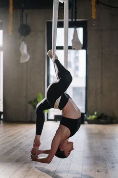 阳光明媚的瑜伽室里，一名女子正表演空中瑜伽，展示着力量与灵活性