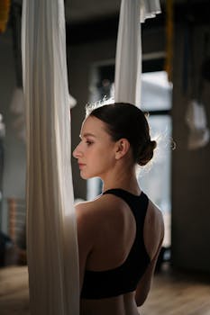 A woman performs aerial yoga in a studio, showcasing grace and focus.
